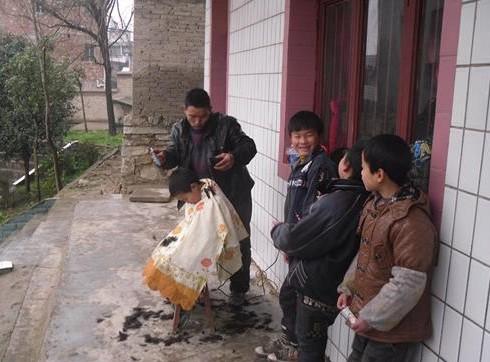 图为残疾人创业代表潘老方正在为留守儿童免费理发