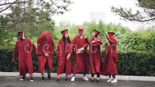 多民族学生穿着长袍和灰泥板在校园户外跳舞欢笑的慢动作短视频