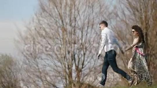 这对幸福的夫妇手牵着手，在群山的背景下沿着草地奔跑的特写镜头。