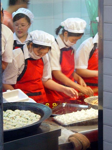 生煎馒头(包子)店里忙碌的厨师们,左面是已出锅的包子,右面是刚包
