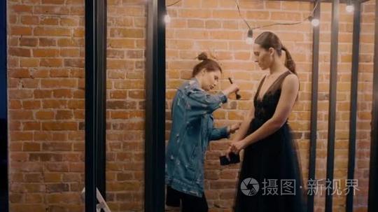专业化妆师在黑色的婚纱让化妆模型。背景下的红砖和白炽灯