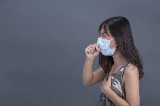 年轻女孩戴着口罩在黑墙上咳嗽_7957211