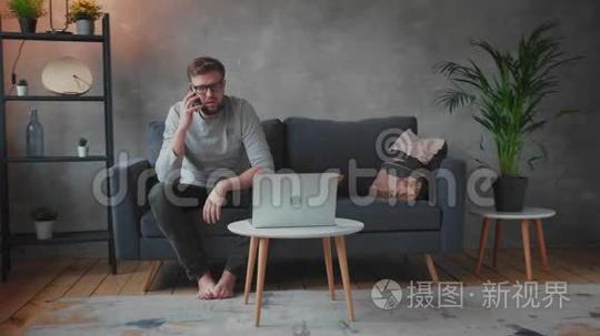 戴眼镜的年轻人生气地坐在沙发上打电话。年轻的商人。