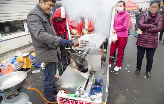 在吉林市的泰和市场，商贩用两个爆米花机来崩栗子，吸引不少市民围观。