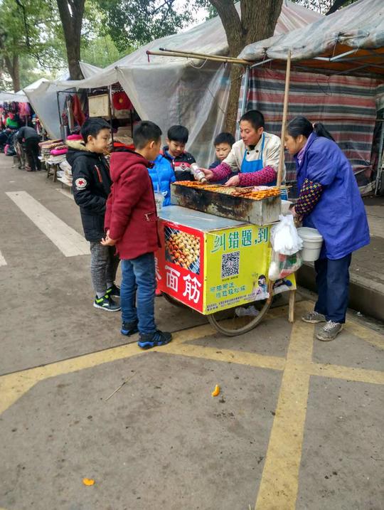 还有烤面筋的小摊,夫妻档合作,一个收钱,一个烤,吸引了很多小学生的