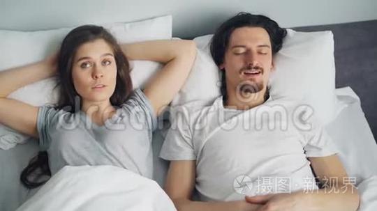 愤怒的妻子一边睡觉一边用枕头遮住脸，丈夫在床上打鼾短视频
